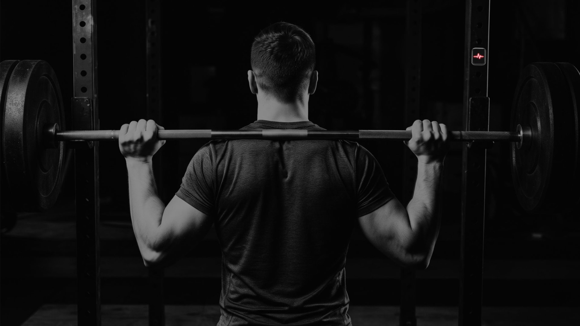 Athlete performing a barbell squat in a gym power rack with the BIT device mounted on the post